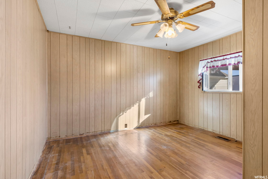 Empty room with hardwood / wood-style floors, wood walls, and ceiling fan