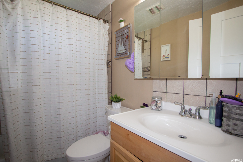 Bathroom featuring toilet, a textured ceiling, tasteful backsplash, vanity with extensive cabinet space, and tile walls