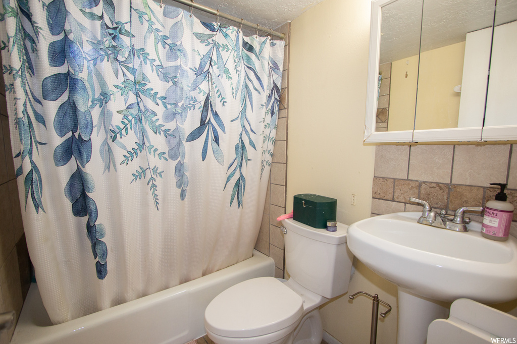Full bathroom with tasteful backsplash, sink, toilet, tile walls, and shower / bathtub combination with curtain