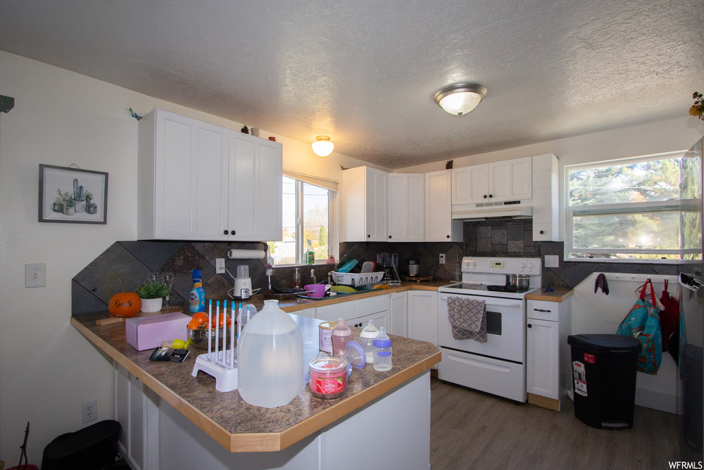 Kitchen featuring tasteful backsplash, kitchen peninsula, white range with electric cooktop, white cabinetry, and dark hardwood / wood-style flooring