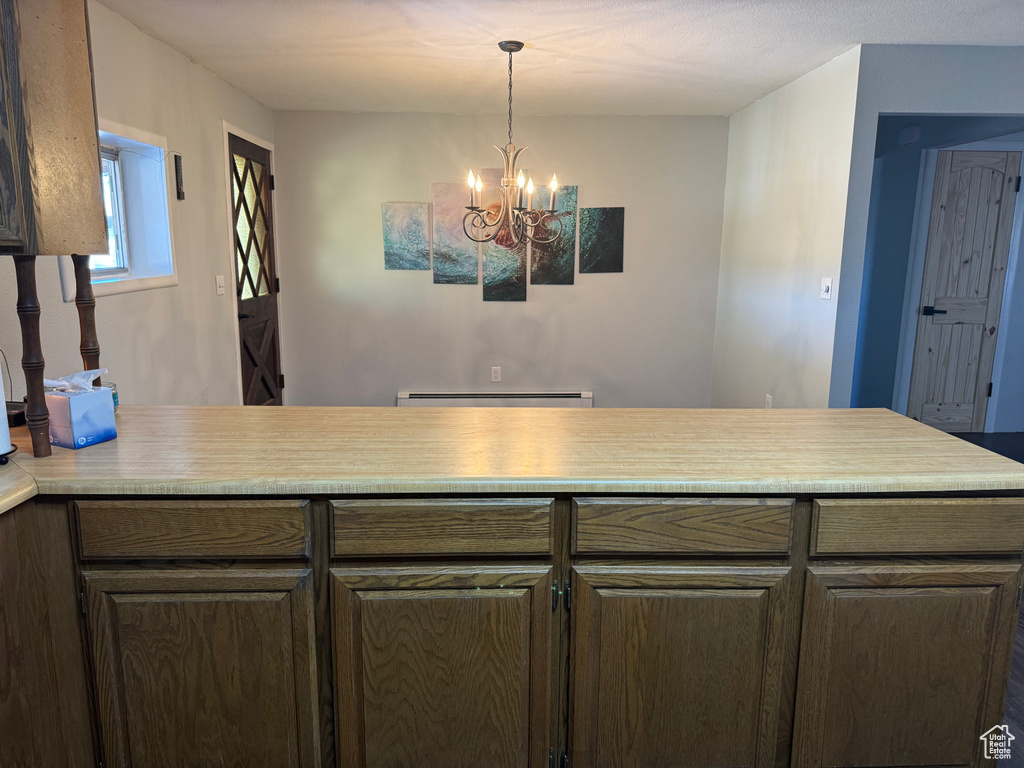 Kitchen with a notable chandelier, kitchen peninsula, a baseboard heating unit, and decorative light fixtures