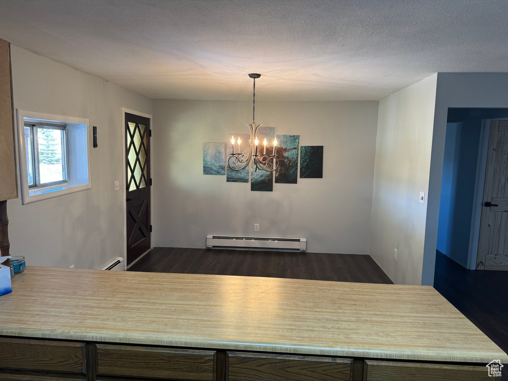 Unfurnished dining area featuring a baseboard radiator, dark hardwood / wood-style flooring, a textured ceiling, and a chandelier