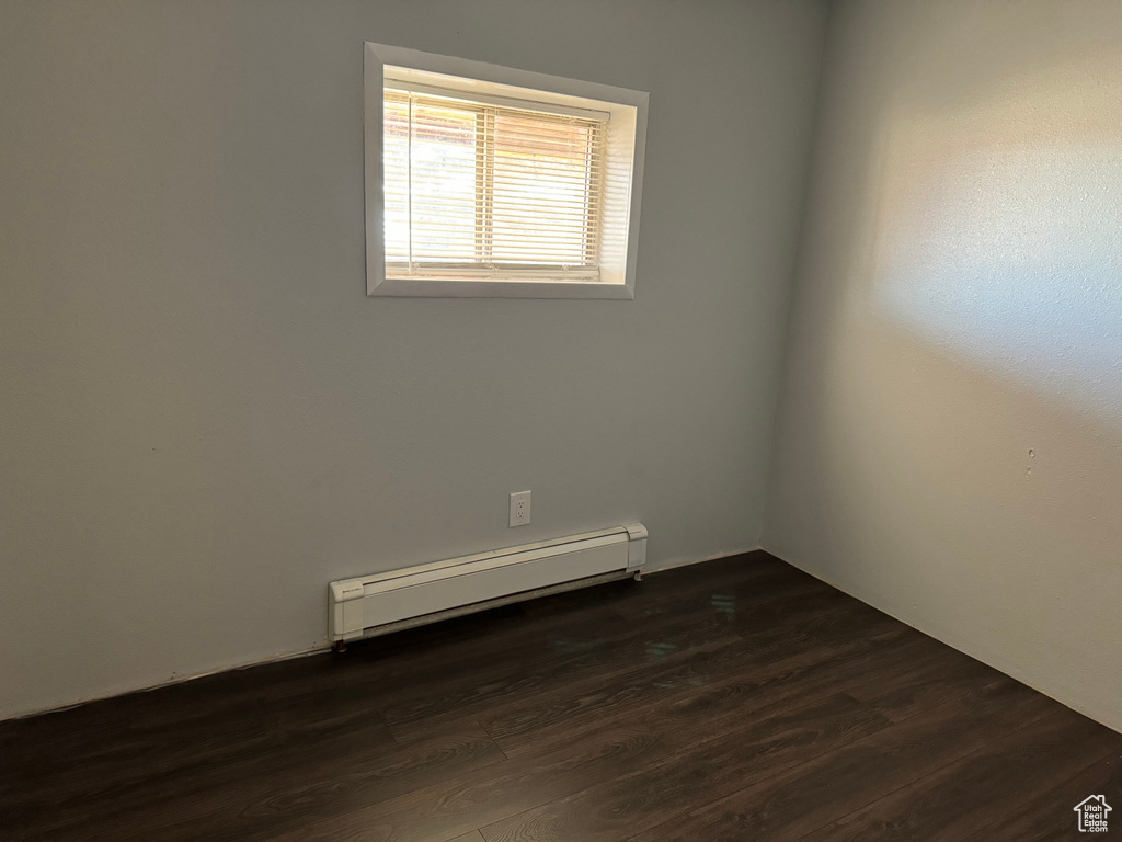 Empty room with dark hardwood / wood-style flooring and a baseboard heating unit