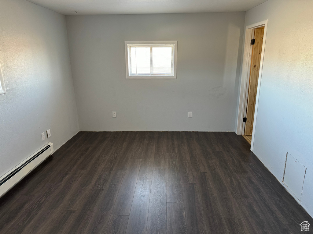 Empty room with dark wood-type flooring and a baseboard heating unit