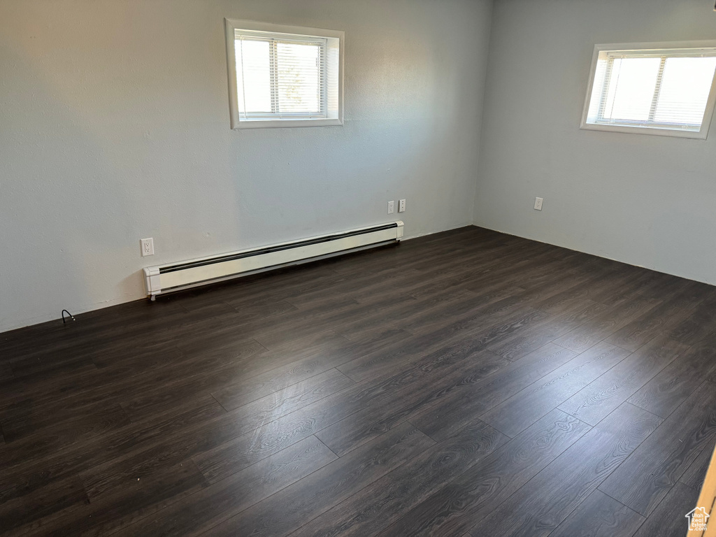 Unfurnished room featuring a baseboard radiator, dark hardwood / wood-style flooring, and a healthy amount of sunlight