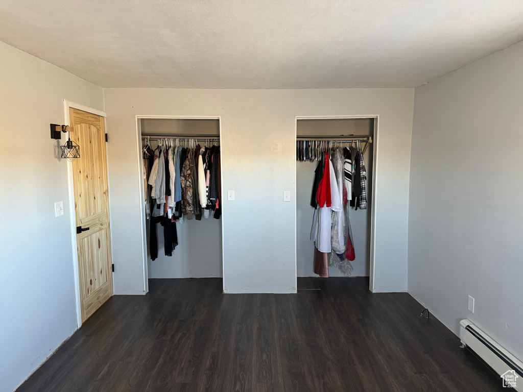Unfurnished bedroom featuring baseboard heating, a closet, and dark wood-type flooring