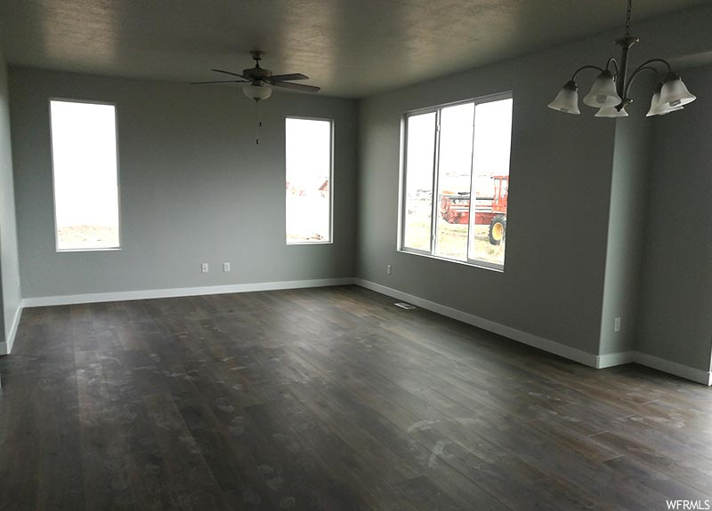 Unfurnished room with dark hardwood / wood-style flooring and ceiling fan with notable chandelier