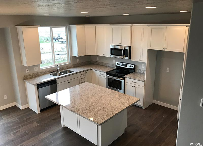 Kitchen featuring sink, a center island, dark wood-type flooring, white cabinets, and appliances with stainless steel finishes