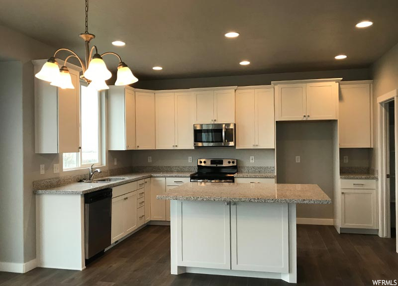 Kitchen featuring a kitchen island, pendant lighting, white cabinetry, stainless steel appliances, and a notable chandelier