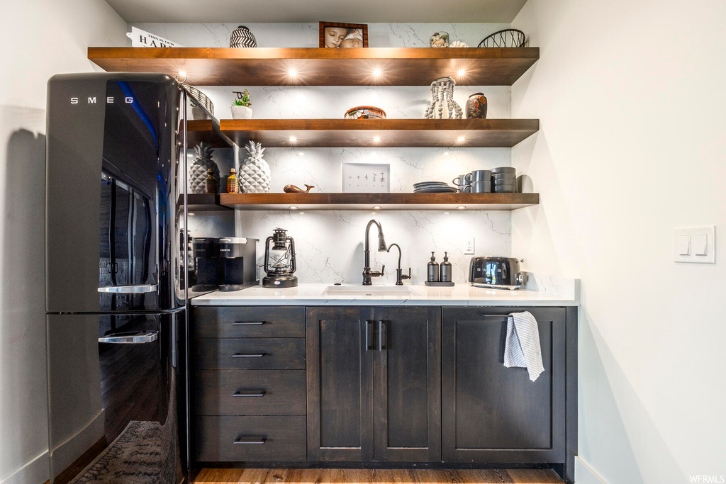 Bar featuring sink, black refrigerator, hardwood / wood-style flooring, dark brown cabinetry, and backsplash