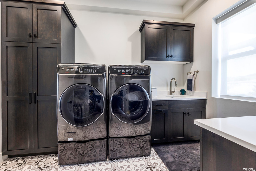 Clothes washing area with light tile flooring, sink, washing machine and clothes dryer, and cabinets