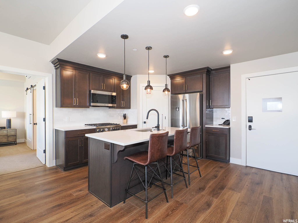 Kitchen featuring decorative light fixtures, sink, stainless steel appliances, dark hardwood / wood-style floors, and a barn door