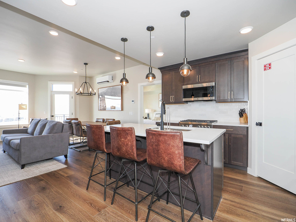 Kitchen featuring dark brown cabinets, a kitchen breakfast bar, a wall mounted AC, dark wood-type flooring, and backsplash