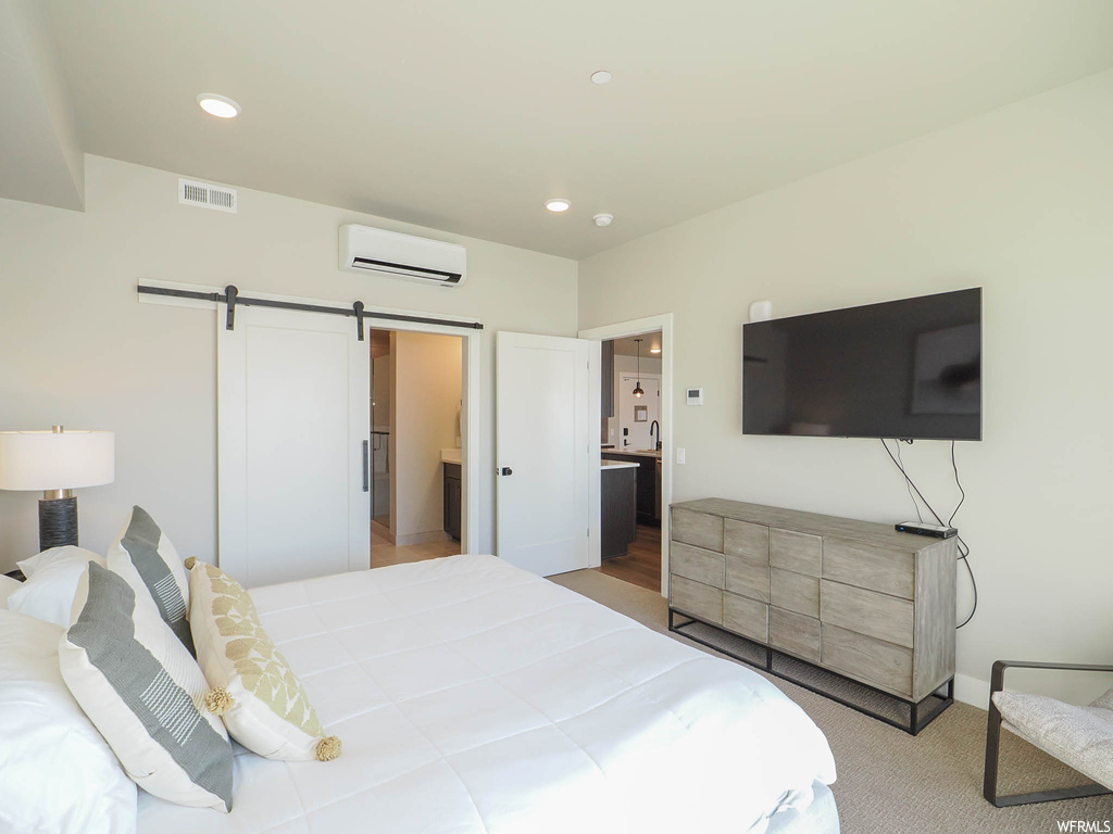 Bedroom featuring connected bathroom, a barn door, an AC wall unit, and light hardwood / wood-style flooring