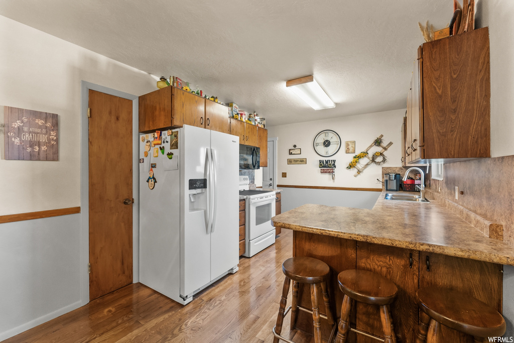 Kitchen with sink, light hardwood / wood-style flooring, backsplash, kitchen peninsula, and white appliances