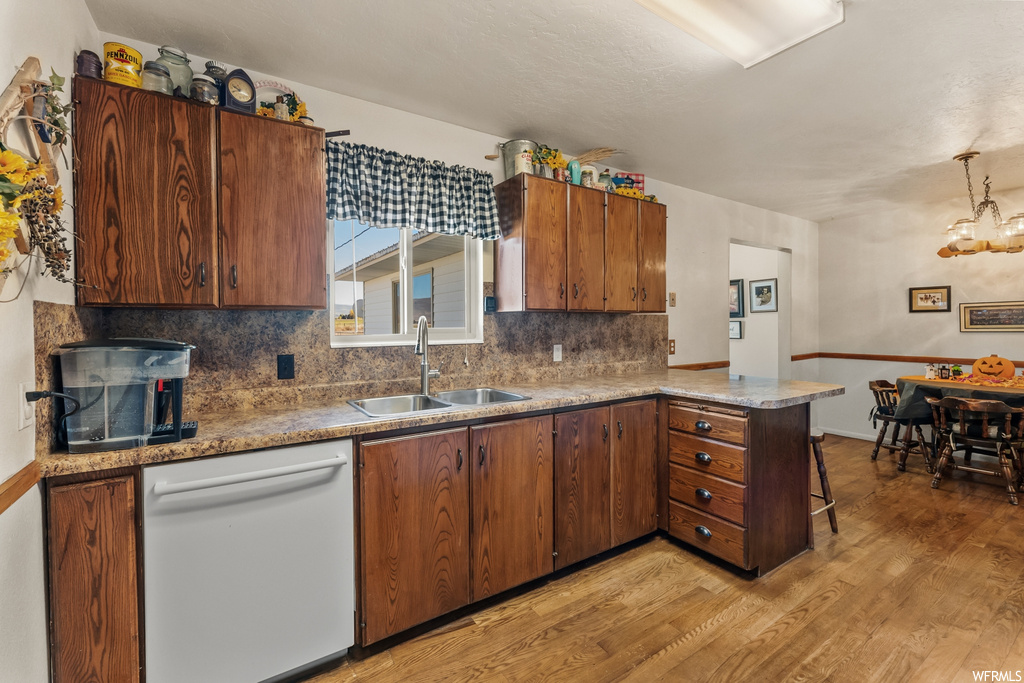 Kitchen with sink, dishwasher, an inviting chandelier, backsplash, and light wood-type flooring