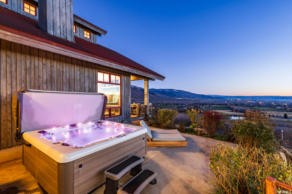 Patio terrace at dusk featuring a mountain view and a hot tub