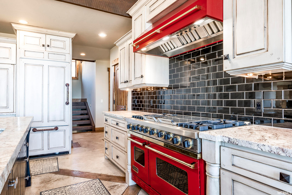 Kitchen featuring premium range hood, range with two ovens, backsplash, light tile floors, and light stone counters