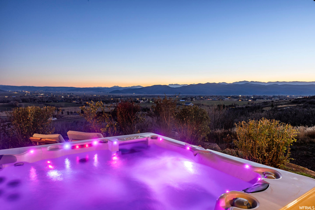 Pool at dusk with a hot tub and a mountain view