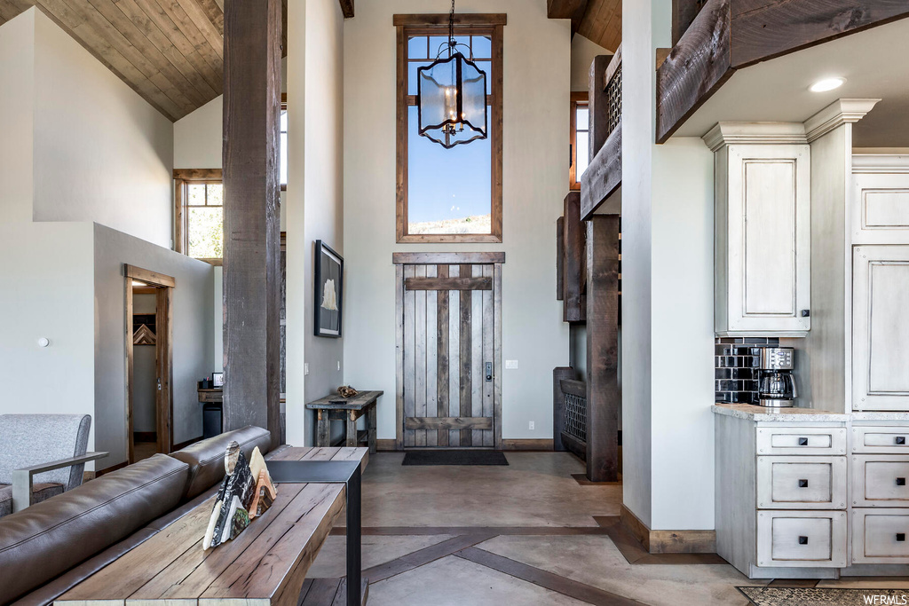 Entryway featuring wood ceiling, high vaulted ceiling, concrete floors, and a notable chandelier