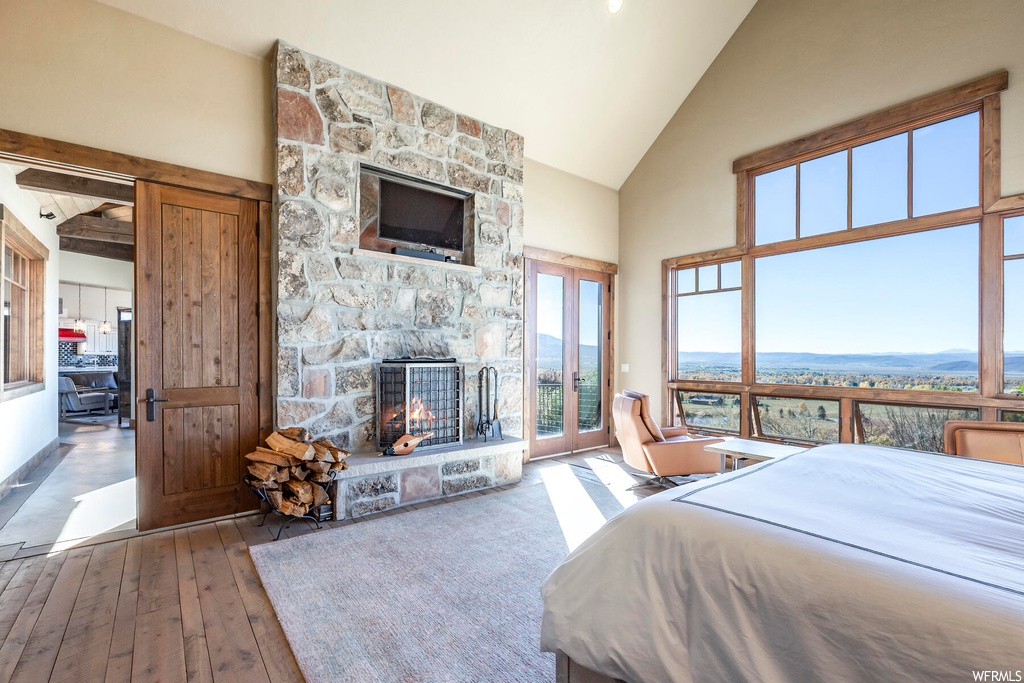 Bedroom featuring light hardwood / wood-style floors, access to outside, a fireplace, and high vaulted ceiling