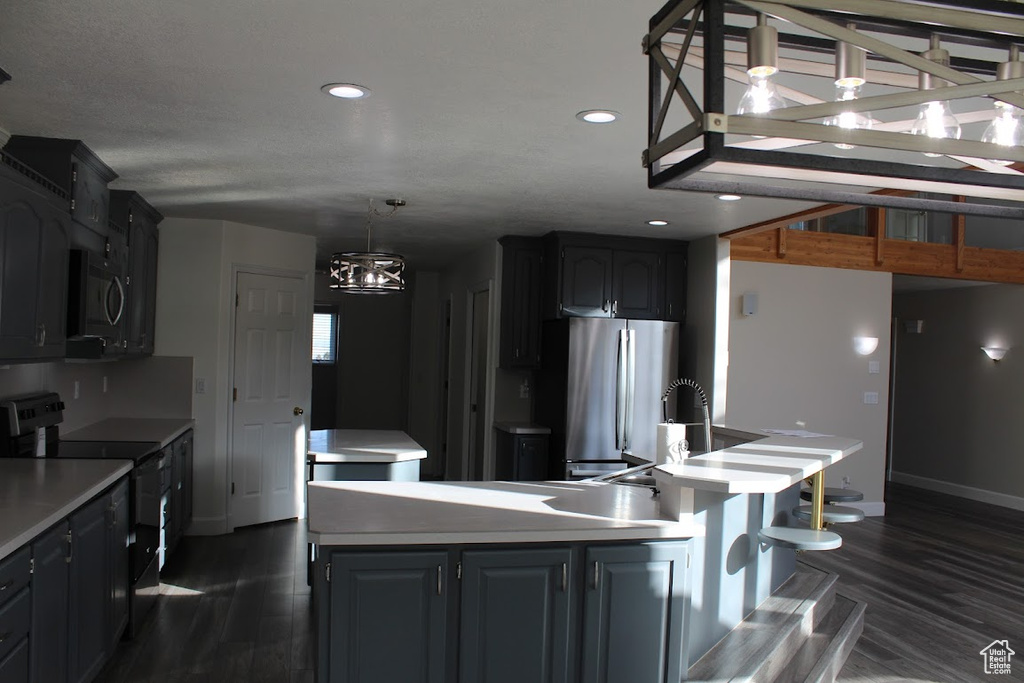 Kitchen with appliances with stainless steel finishes, hanging light fixtures, dark wood-type flooring, gray cabinetry, and a center island with sink