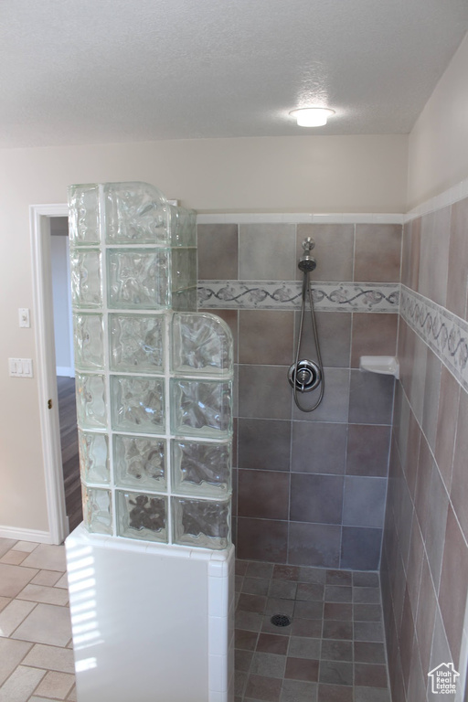 Bathroom featuring a textured ceiling, a tile shower, and tile floors