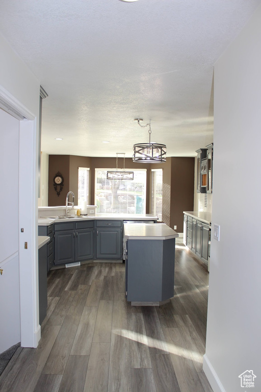 Kitchen featuring dark wood-type flooring, a kitchen island, gray cabinets, pendant lighting, and sink
