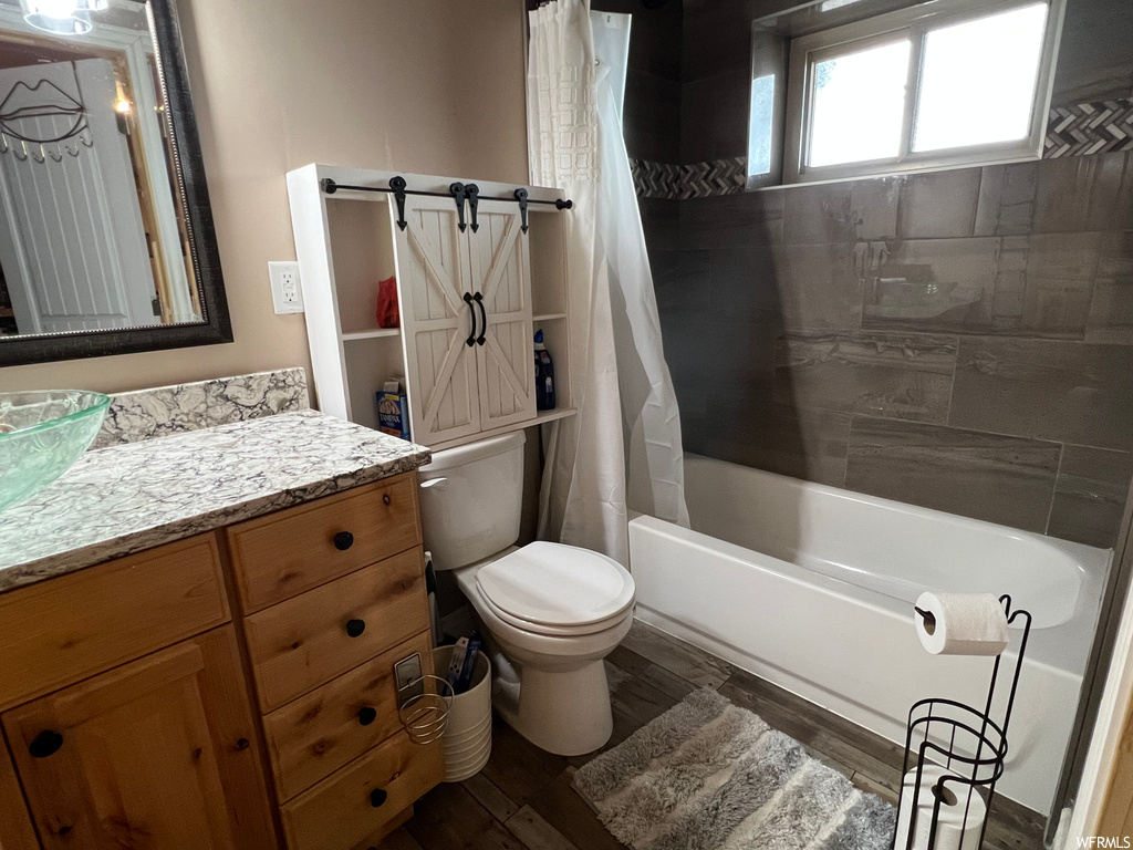 Full bathroom featuring wood-type flooring, shower / bathtub combination with curtain, vanity, and toilet