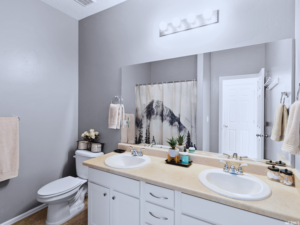 Bathroom with dual vanity, a textured ceiling, and toilet
