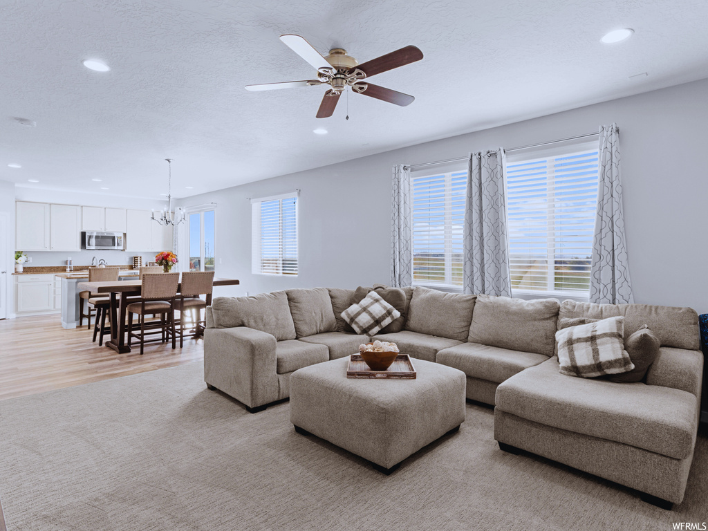 Living room featuring ceiling fan with notable chandelier and light hardwood / wood-style flooring