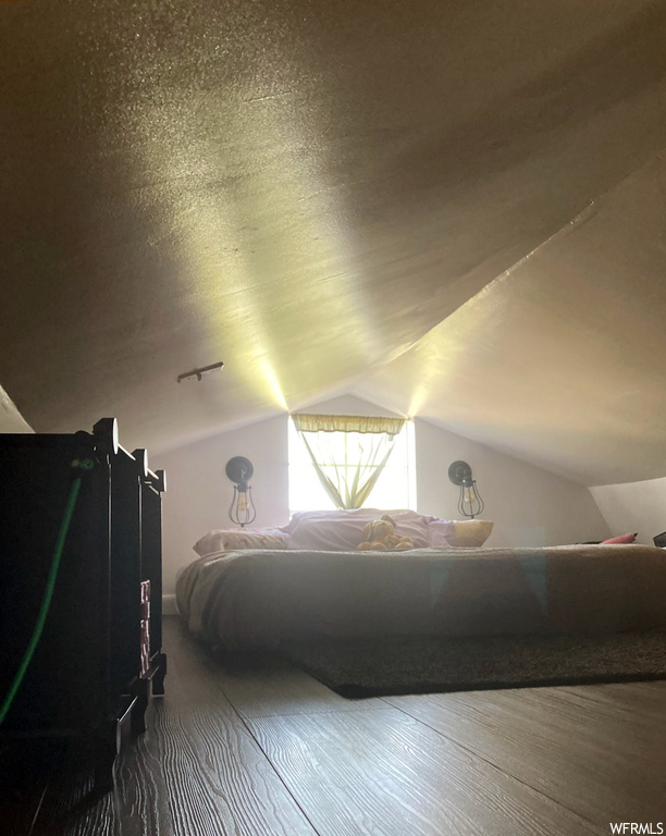 Hardwood floored bedroom featuring lofted ceiling and a textured ceiling