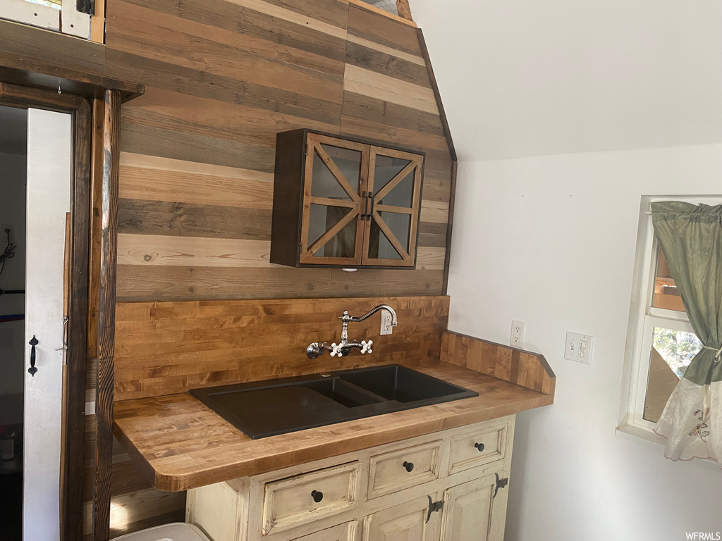 Kitchen featuring cream cabinetry, wood walls, backsplash, and sink