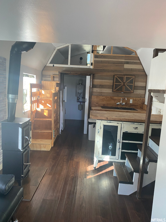 Interior space with a wood stove, wood walls, vaulted ceiling, and dark hardwood / wood-style floors