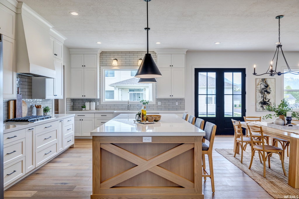Kitchen with tasteful backsplash, a center island, light hardwood / wood-style floors, white cabinets, and pendant lighting
