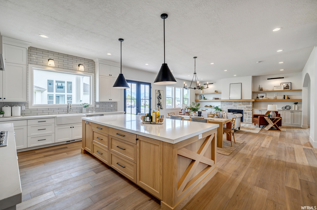 Kitchen featuring a center island, light wood-type flooring, a fireplace, a notable chandelier, and pendant lighting
