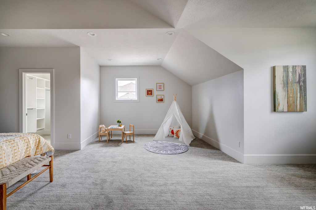 Recreation room featuring vaulted ceiling, a textured ceiling, and light colored carpet