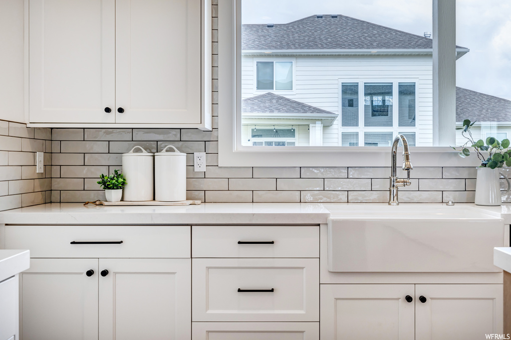Kitchen featuring tasteful backsplash, white cabinets, and light stone countertops