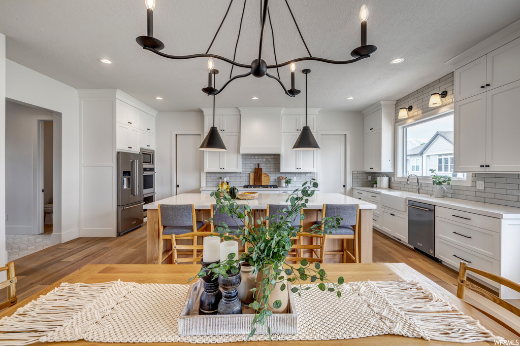 Kitchen with a center island, decorative light fixtures, appliances with stainless steel finishes, white cabinetry, and light wood-type flooring