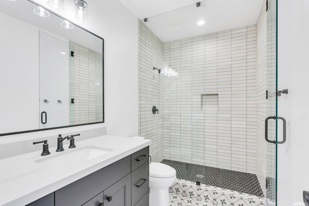 Bathroom featuring tile flooring, a shower with shower door, toilet, and oversized vanity