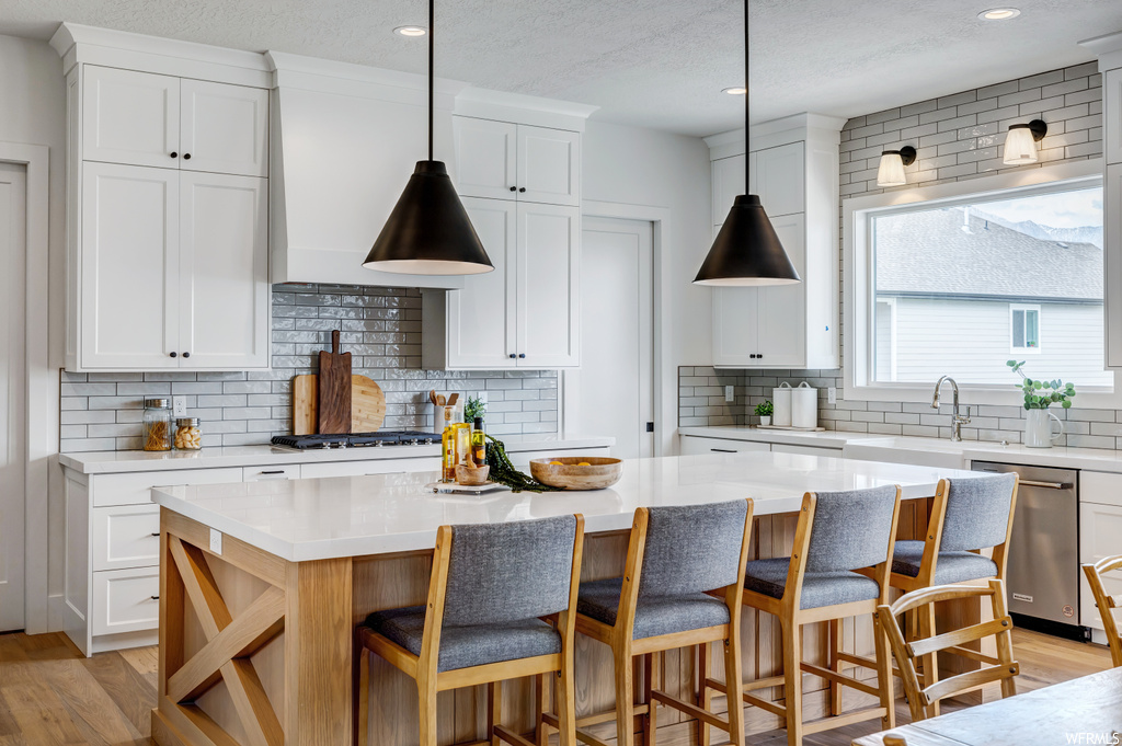 Kitchen with hanging light fixtures, a center island, backsplash, white cabinets, and appliances with stainless steel finishes