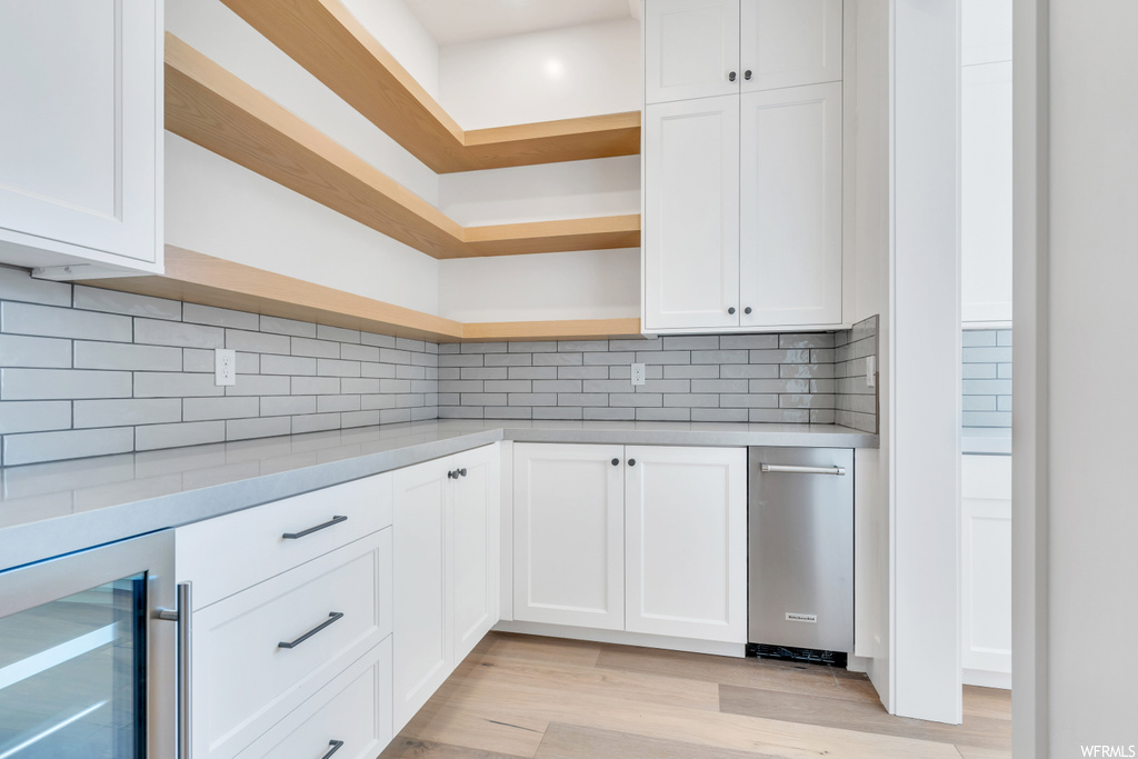 Kitchen with light wood-type flooring, tasteful backsplash, beverage cooler, and white cabinets