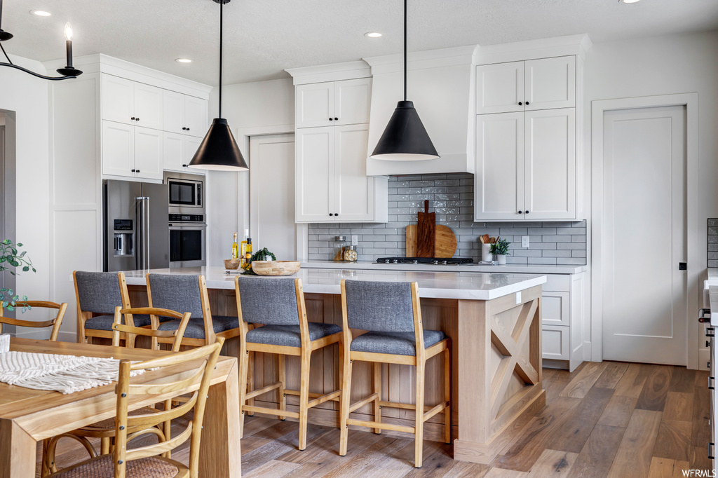 Kitchen featuring decorative light fixtures, a kitchen island with sink, white cabinetry, and dark hardwood / wood-style floors
