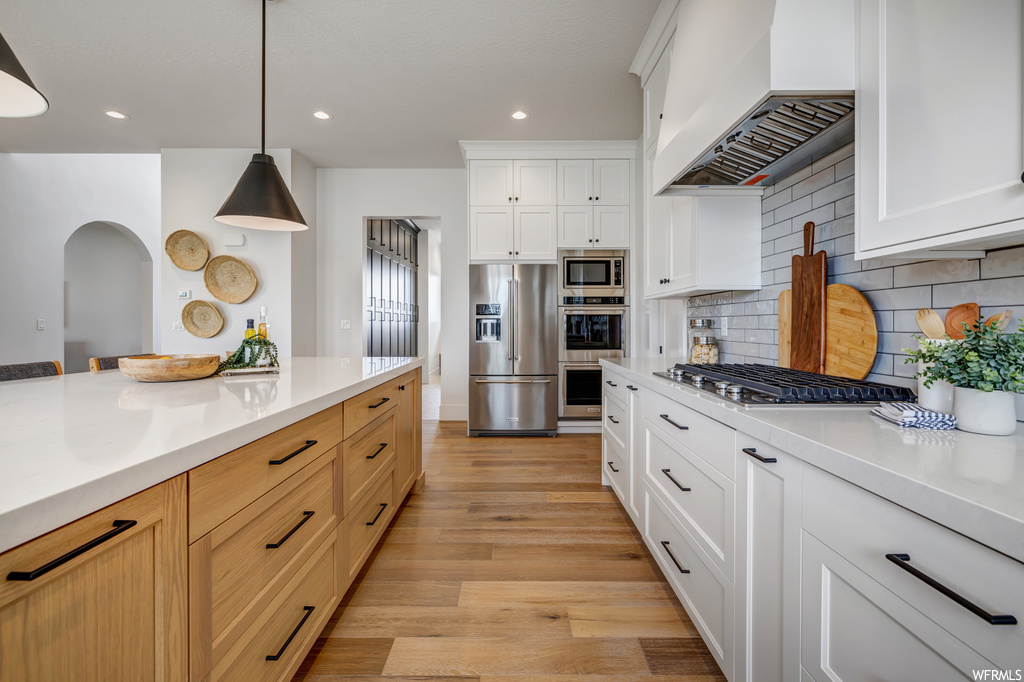 Kitchen with light hardwood / wood-style floors, custom range hood, tasteful backsplash, white cabinetry, and pendant lighting