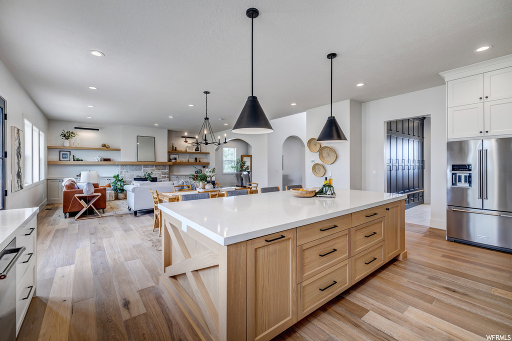 Kitchen with light hardwood / wood-style flooring, hanging light fixtures, a center island, a chandelier, and appliances with stainless steel finishes
