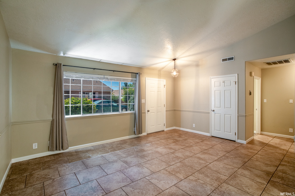 Empty room with vaulted ceiling and light tile floors