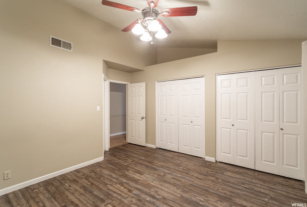 Unfurnished bedroom with two closets, dark hardwood / wood-style flooring, ceiling fan, and vaulted ceiling
