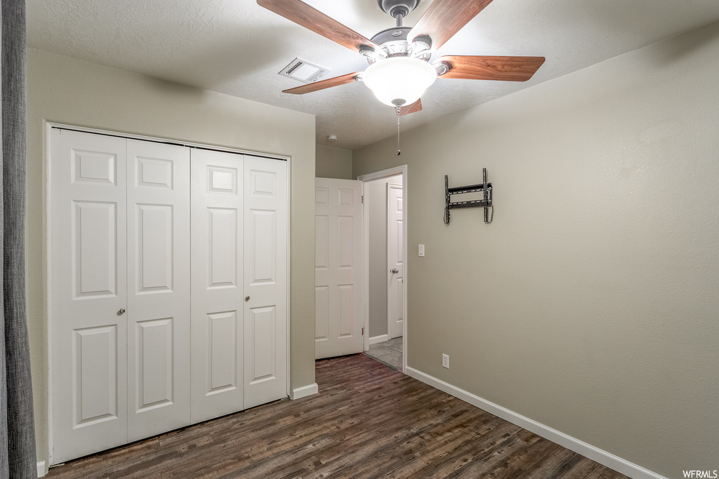 Unfurnished bedroom with ceiling fan, dark hardwood / wood-style flooring, and a closet