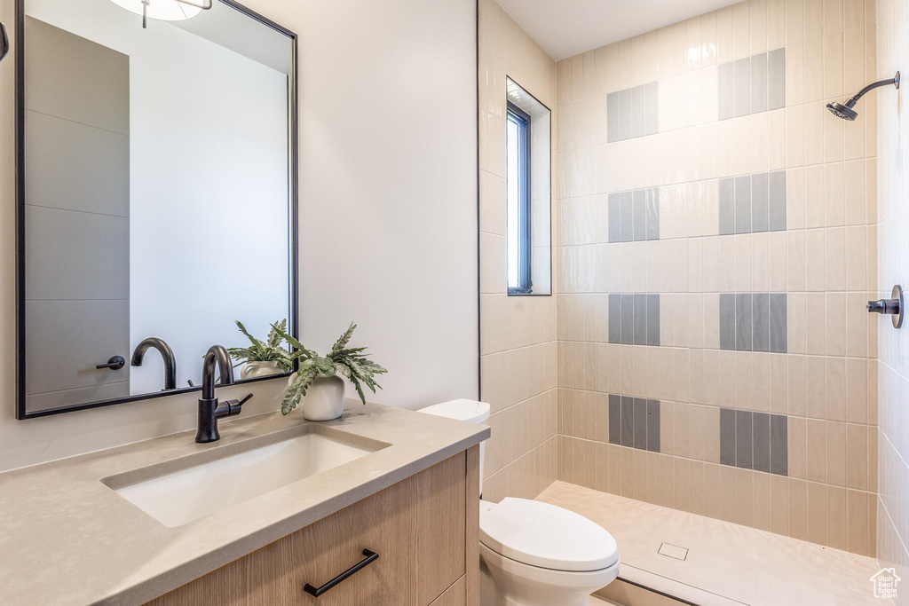 Bathroom featuring a tile shower, vanity, and toilet