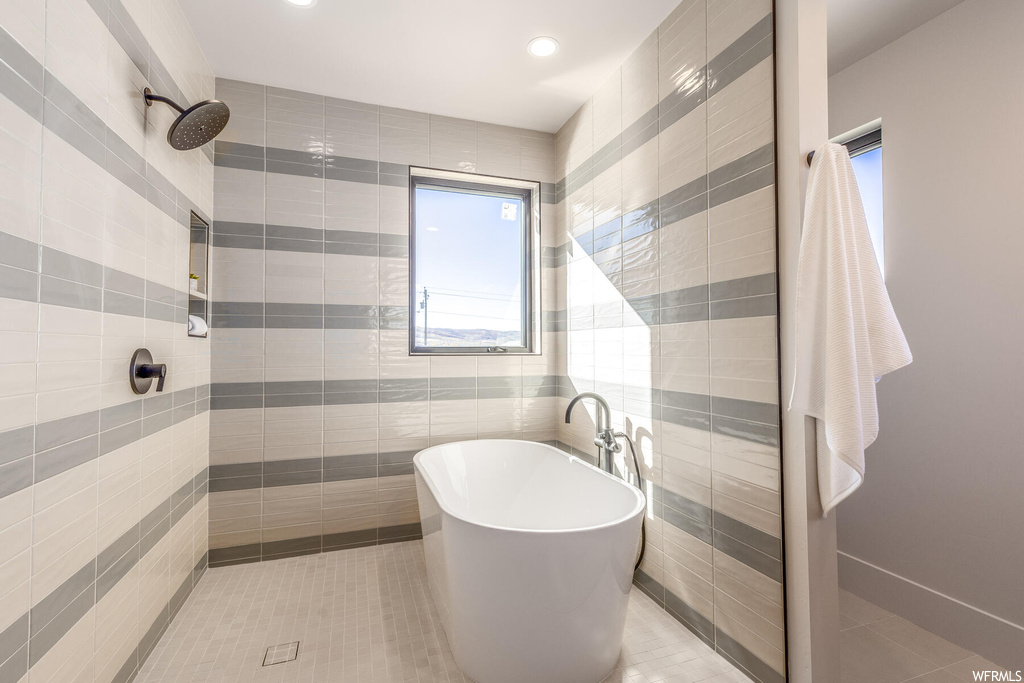 Bathroom with plenty of natural light, tile flooring, separate shower and tub, and tile walls